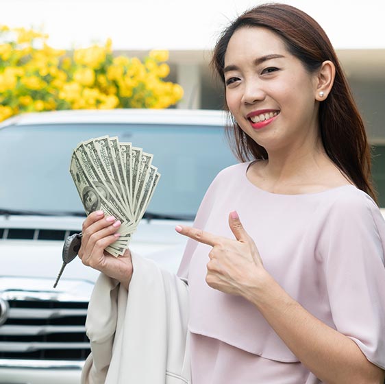 A picture of a smiling woman pointing at cash in hand, standing in front of a truck