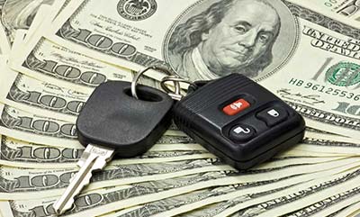 A set of car keys sitting on a group of neatly fanned out $100 bills