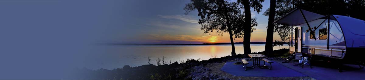 A picture of an RV that is parked at a lakeside campsite at sunset