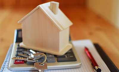 A tiny wooden model of a home sitting on top of a calculator