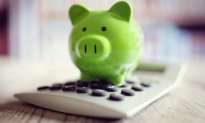 A small green piggy bank is standing on top of a calculator