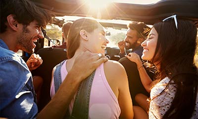 A group of people laughing while they ride into the sunset in a vehicle that has the top off.