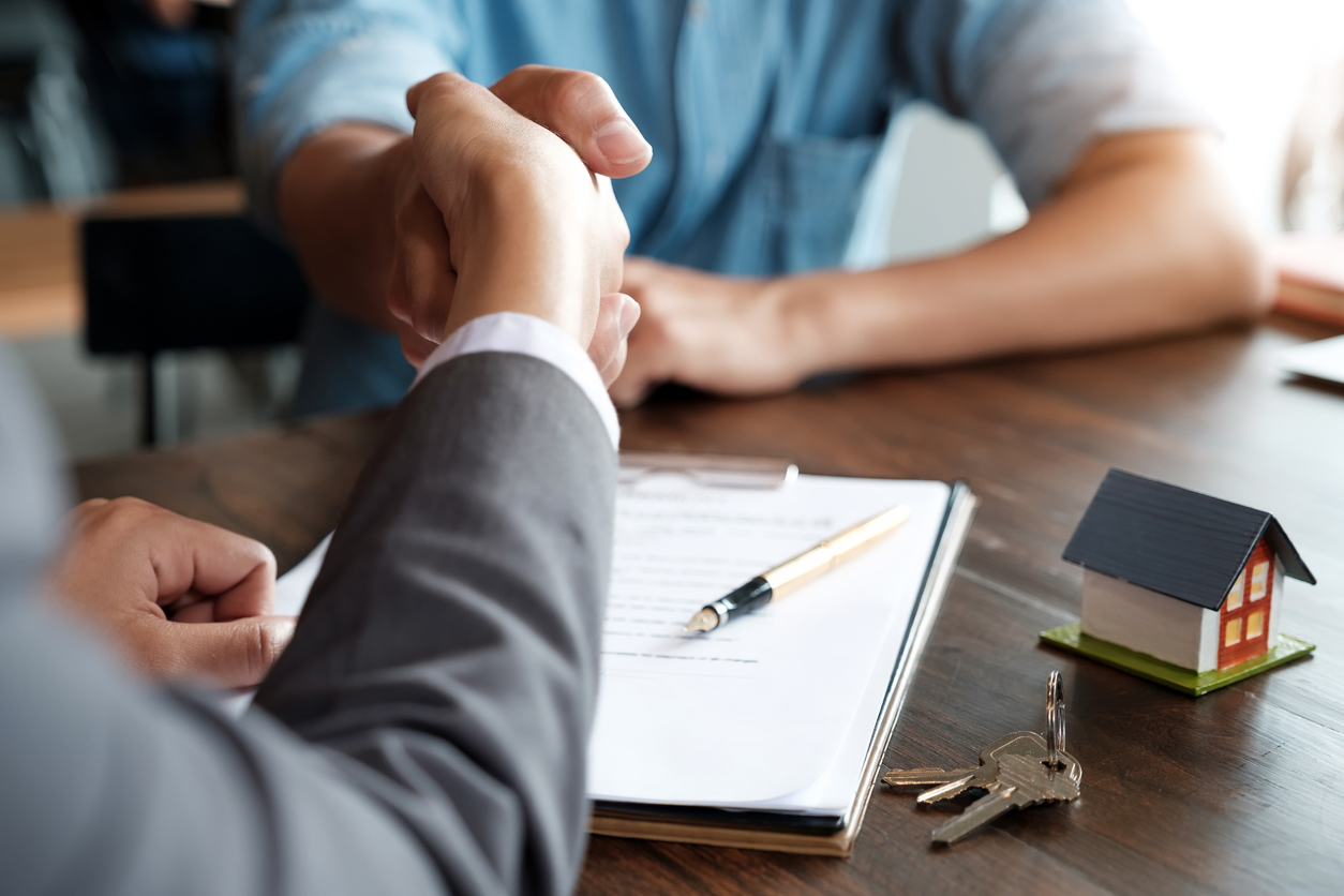 Two people shaking hands with keys on the table