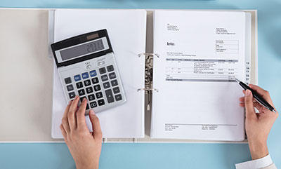 A first person view of working with a calculator, pen and folder on a blue desk.