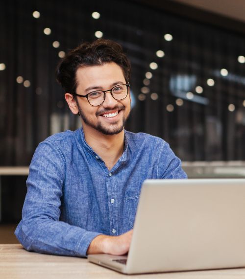 A smiling man sitting at a desk that has an open laptop on it