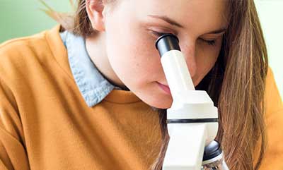 A close up of a student looking into a microscope