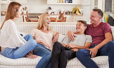 A mother, father, daughter and son sitting together on a couch, all smiling and laughing.