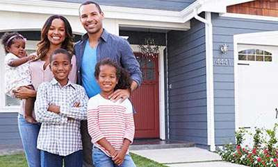 A family standing in a font yard, all smiling and posing for a picture with a home in the background